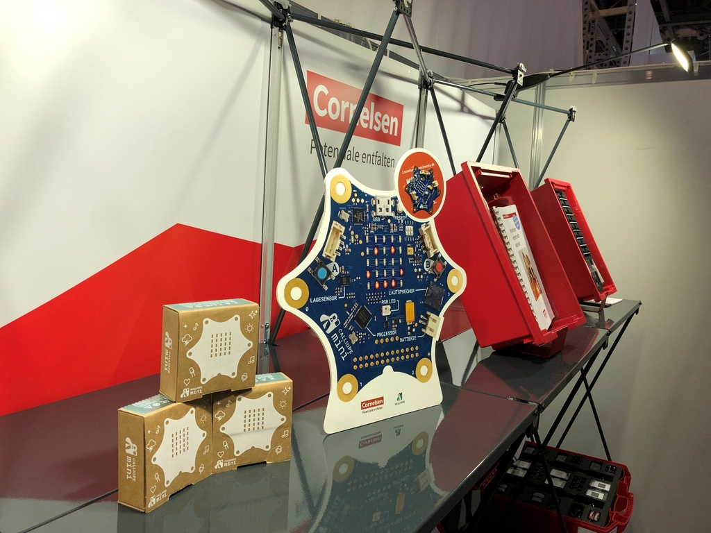 Das Bild zeigt einen Messestand mit verschiedenen Lehrmaterialien für das deutsche Bildungswesen. Im Vordergrund ist eine Schaltung zu sehen, umgeben von gestapelten Boxen mit zusätzlichen Geräten oder Modulen.