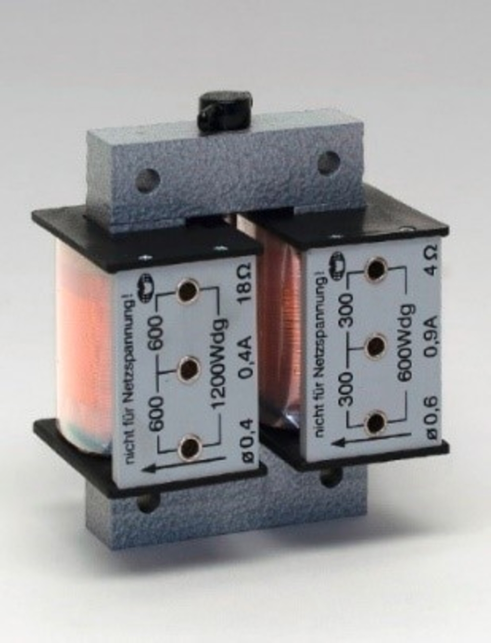 Das Bild zeigt eine elektrische Spule mit zwei Wicklungen, die auf einer stabilen Basis montiert ist. Die Spule verfügt über mehrere Anschlüsse, die für Experimente im Bereich der Elektrotechnik und Physik genutzt werden können.