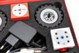 Das Bild zeigt eine Werkzeugbox mit verschiedenen Bauteilen für ein Experimentierset, darunter ein Motor, Räder und Steuerungselemente. Diese Teile sind in einer gepolsterten Halterung angeordnet und bieten Möglichkeiten für praktische Experimente im Bild