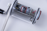 Das Bild zeigt ein transparentes Gerät mit einem Elektromotor und einem Getriebe, das für experimentelle Zwecke konstruiert ist. Es verfügt über eine Halterung und verschiedene Anschlussdrähte, die für den Betrieb und die Montage erforderlich sind.