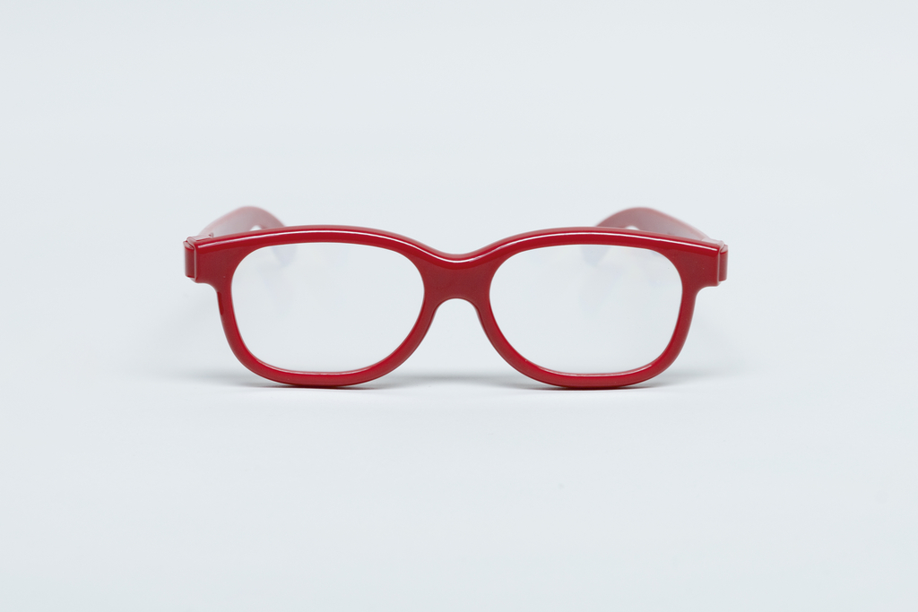 Das Bild zeigt eine rote Brille mit klaren Gläsern, die zentral auf einem weißen Hintergrund platziert ist. Sie ist für experimentelle Bildungszwecke konzipiert und könnte in Schulen oder für wissenschaftliche Anwendungen verwendet werden.