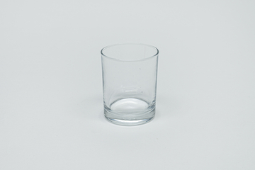 Das Bild zeigt ein transparentes Glas, das in einem neutralen Umfeld fotografiert wurde. Es handelt sich um ein einfaches, zylindrisches Gefäß, das für Experimente im Bildungsbereich verwendet werden kann.