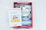Das Bild zeigt einen roten Kasten mit Experimentiermaterialien für Kinder, einschließlich Pipetten, Gläsern und einem Begleitbuch. Das Buch thematisiert Experimente mit Licht und Schall und richtet sich an den Kindergartenbereich.