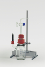 Das Bild zeigt ein chemisches Experimentiergerät, das aus einem Glasgefäß mit roten Schraubverschlüssen und verschiedenen Glasrohren besteht. Es ist auf einem stabilen Ständer montiert und dient zur Durchführung von Experimenten im Bildungsbereich.