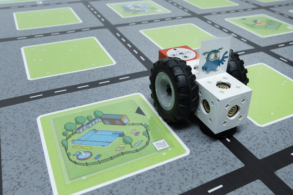 Detailbild von dem eXperiBot auf dem Spielplan für die Grundschule. Der eXperiBot steht neben dem Schwimmbad und kann über Programmierung zu anderen Orten auf dem Spielplan gelangen.