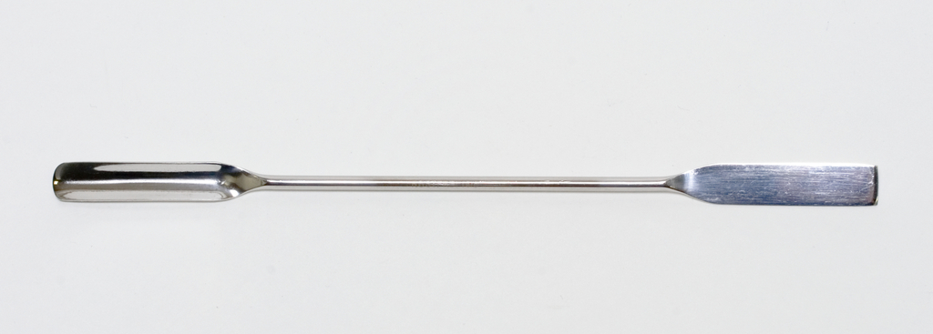 Das Bild zeigt ein langes, flaches, metallisches Werkzeug mit einem breiten Ende, das zum Mischen oder Umrühren von Substanzen verwendet wird. Es ist vermutlich für den Einsatz in Experimenten oder im Laborumfeld konzipiert.
