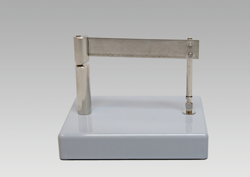 Das Bild zeigt ein Experimentiergerät auf einem grauen Sockel, das aus verchromtem Metall besteht. Es hat einen drehbaren Arm, der vermutlich für physikalische Experimente oder Demonstrationen genutzt werden kann.
