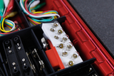 Das Bild zeigt ein Set von elektronischen Bauteilen, das in einem roten Kasten angeordnet ist. Darunter befinden sich mehrere bunte Kabel und eine Reihe von Lampenelementen, die für experimentelle Anwendungen im Bildungsbereich genutzt werden können.