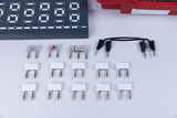 Das Bild zeigt eine Anordnung von verschiedenen Steckverbindern und Bauteilen auf einem Tisch. Im Hintergrund ist eine Experimentiervorlage mit mehreren Löchern zu sehen, die zur Durchführung von elektronischen Experimenten verwendet werden kann.