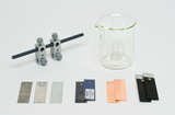 Das Bild zeigt verschiedene experimentelle Materialien, darunter zwei Halterungen mit einer Stange, einen Becher und mehrere Metallplatten in unterschiedlichen Farben und Oberflächen. Diese Materialien sind typischerweise für chemische oder physikalische Experimente im Bildungsbereich vorgesehen.