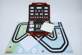 Das Bild zeigt einen roten Koffer, der mit verschiedenen Experimentiermaterialien gefüllt ist, sowie ein farbenfrohes Spielfeld mit Straßenmustern und QR-Codes. Der Koffer enthält Komponenten für praktische Experimente, die das Lernen im Bildungsbereich unterstützen sollen.