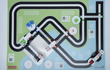 Das Bild zeigt eine farbige Spielmatte mit einer verzweigten Straßenführung sowie mehreren Stationen, die mit Zahlen und QR-Codes gekennzeichnet sind. Modelle von Fahrzeugen sind auf der Matte platziert, was auf eine interaktive Lernumgebung hinweist.
