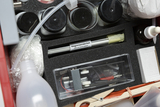 Der Inhalt umfasst verschiedene Behälter mit Materialien, eine Pipette und eine Box mit einem elektrischen Bauteil. Zudem sind ein paar Magnesiastäbchen und diverse weitere experimentelle Hilfsmittel sichtbar, die für den naturwissenschaftlichen Unterricht verwendet werden können.