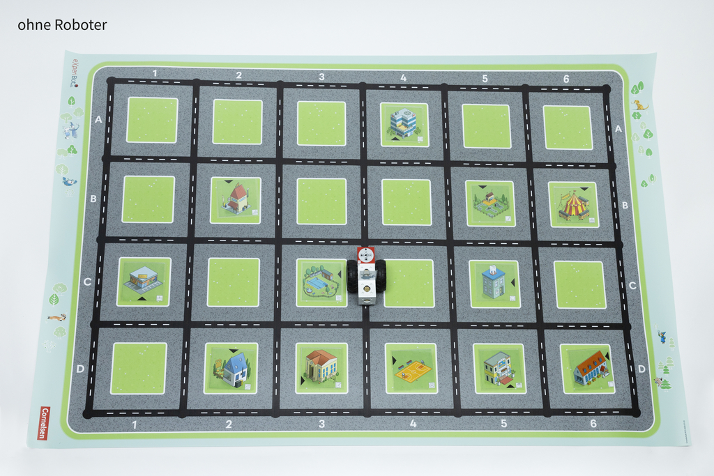 Auf einer bunten Matte ist ein Spielfeld mit einem Schachbrettmuster und verschiedenen stilisierten Gebäuden abgebildet. Eine kleine Figur oder ein Roboter befindet sich in der Mitte und kann auf den Straßen bewegt werden, um die Umgebung zu erkunden.