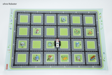 Auf einer bunten Matte ist ein Spielfeld mit einem Schachbrettmuster und verschiedenen stilisierten Gebäuden abgebildet. Eine kleine Figur oder ein Roboter befindet sich in der Mitte und kann auf den Straßen bewegt werden, um die Umgebung zu erkunden.