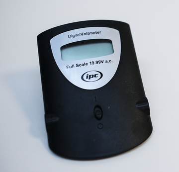 Ein Digitalvoltmeter ist abgebildet, das für die Messung von Wechselspannung bis zu 19,99 V ausgelegt ist. Es hat ein schwarzes Gehäuse mit einem klaren Display und mehreren Bedienelementen.