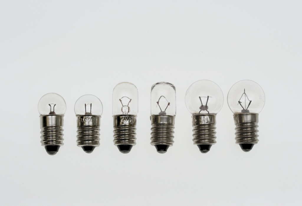 Sechs verschiedene Glühbirnen mit Schraubsockel sind auf einer weißen Fläche angeordnet. Die Birnen variieren in Größe und Form und zeigen die unterschiedlichen inneren Strukturen, die für ihre Funktion als Lichtquelle verantwortlich sind.
