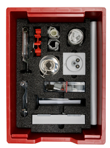 In einer roten Aufbewahrungsbox befinden sich verschiedene Experimentiermaterialien, darunter Gläser, Rohre, eine experimentelle Apparatur und Schutzausrüstung. Die Anordnung der Gegenstände in Schaumstoff sorgt für sicheren Halt und Ordnung.