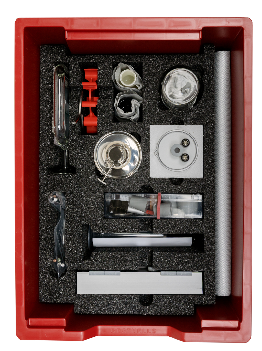 In einer roten Aufbewahrungsbox befinden sich verschiedene Experimentiermaterialien, darunter Gläser, Rohre, eine experimentelle Apparatur und Schutzausrüstung. Die Anordnung der Gegenstände in Schaumstoff sorgt für sicheren Halt und Ordnung.