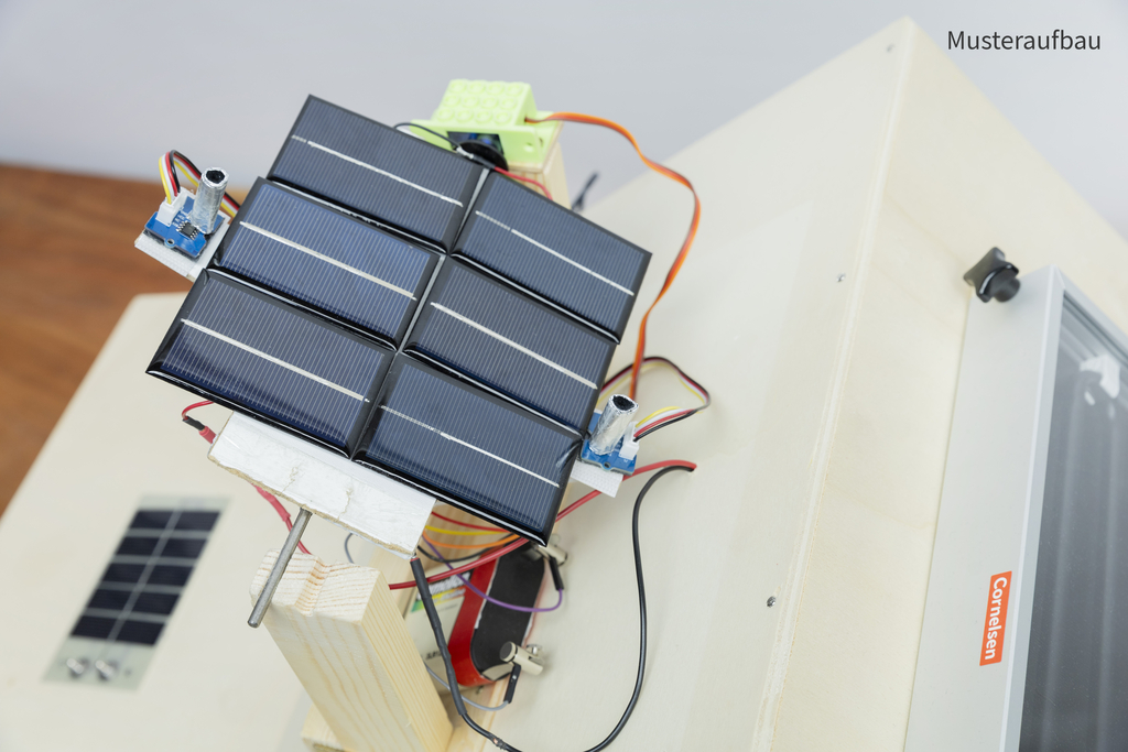 Auf einer Holzplatte sind mehrere Solarzellen angeordnet, die mit bunten Kabeln verbunden sind. Neben den Solarzellen befinden sich elektronische Komponenten, wahrscheinlich für Experimente zur Umwandlung von Sonnenenergie.