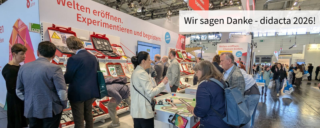 Ein Stand auf einer Messe zeigt verschiedene Experimentierkästen und Lehrmaterialien für den Bildungsbereich. Fachleute und Besucher interagieren und erkunden die Angebote, während ein Banner "Wir sagen Danke - didacta 2026!" sichtbar ist.