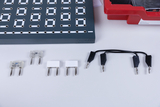Zu sehen sind verschiedene elektrische Bauteile, darunter Widerstände und Verbindungsdrähte, die für Experimente in der Elektronik verwendet werden. Diese Komponenten liegen auf einem hellen Untergrund und sind gut organisiert, um die Nutzung zu erleichtern.